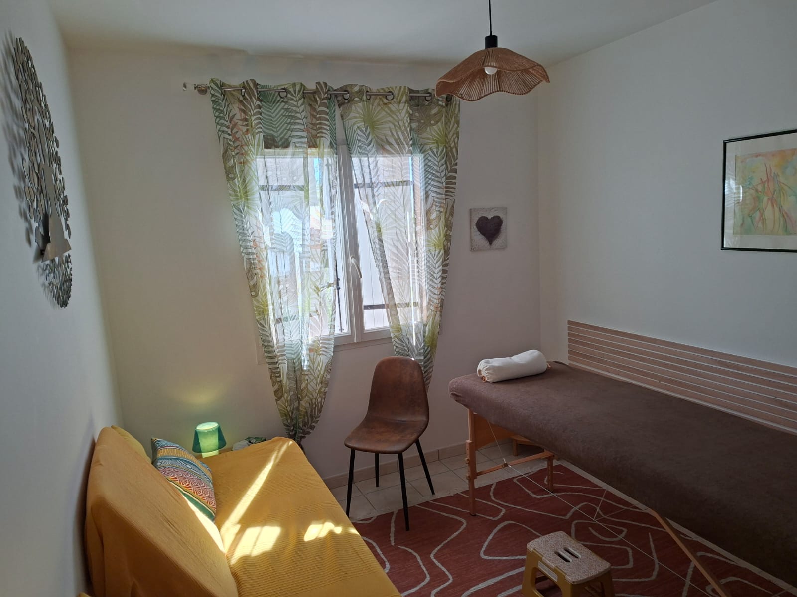 Le cabinet du Puy de Lignac à Saint-Androny : table de massage, canapé et fenêtre donnant sur le jardin